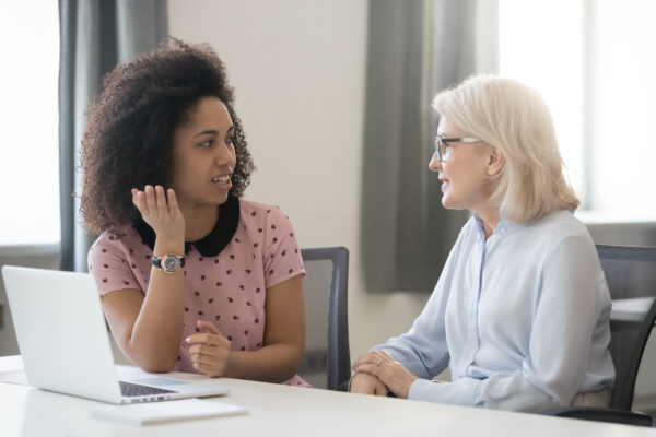 A young woman sat at a desk talking with an older woman