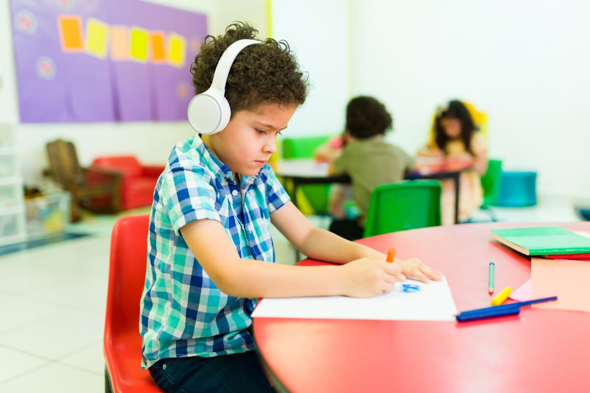 Young boy with black curly hair and earphones not enjoying class
