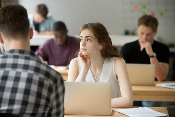 Student sat at desk in class distracted and looking away while classmates get on with work