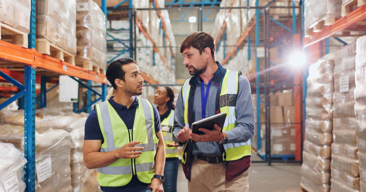 2 men in hi-vis vests walking through warehouse