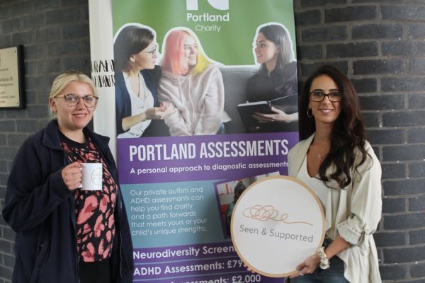 a blonde woman with glasses holding a mug and a brunette lady holding a sign