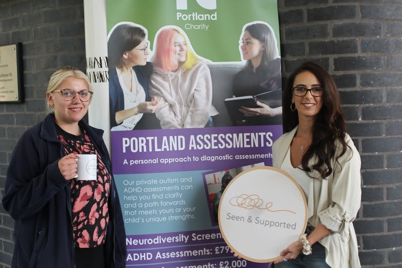 a blonde woman with glasses holding a mug and a brunette lady holding a sign