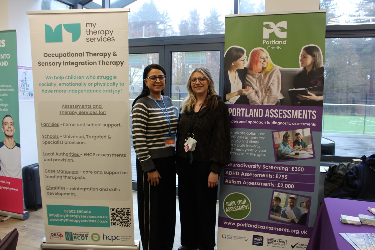 A blonde woman and brunette woman stood smiling in front of banner stands