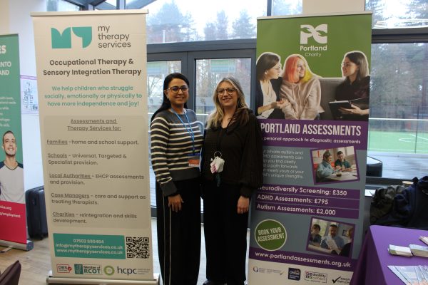 A blonde woman and brunette woman stood smiling in front of banner stands